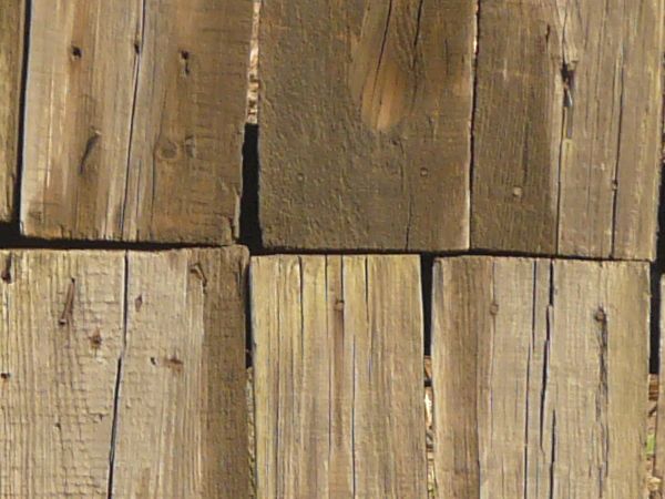 Uneven brown planks with crooked edges and dark spots set vertically with large gaps in between.